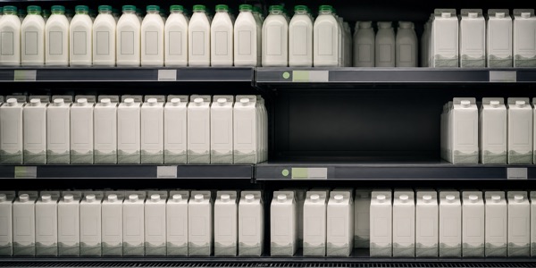 Supermarket dairy shelves with a visible low-stock gap among the milk cartons